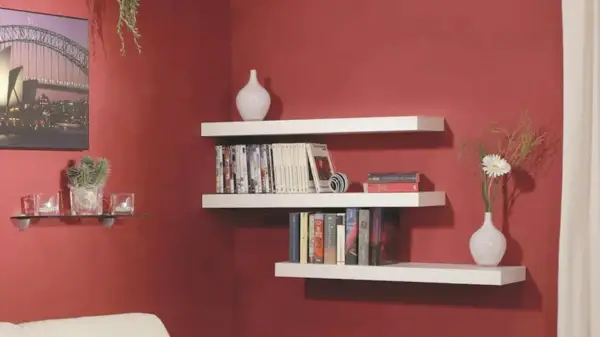 Mensole bianche a muro con libri, vasi e una pianta. Una guida visiva su come montare una mensola.