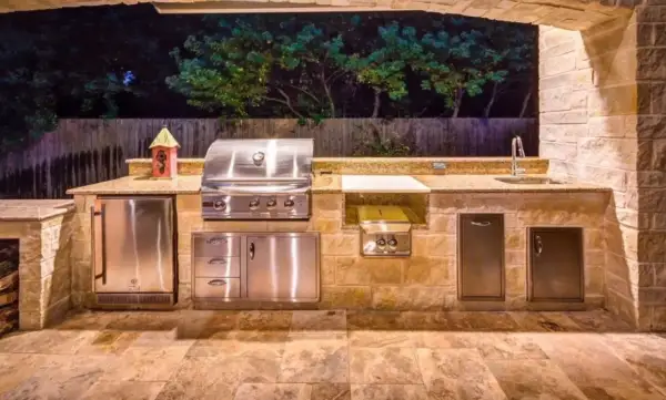 Cucina esterna in muratura fai da te con barbecue, frigo, lavello e piano di lavoro in granito.