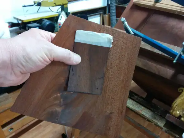 Mano che tiene un pezzo di impiallacciatura di legno scuro, pronto per restaurare un mobile impiallacciato.
