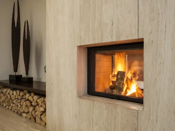 Un camino moderno con fiamme vive, pronto per lo spazzacamino. Legna accatastata e sculture decorative completano l'arredo.