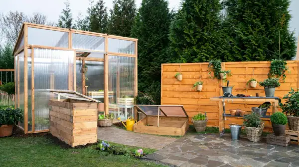 Un giardino con una serra in legno e policarbonato, un banco da lavoro e un'aiuola rialzata. Ideale per chi vuole imparare come costruire una serra.