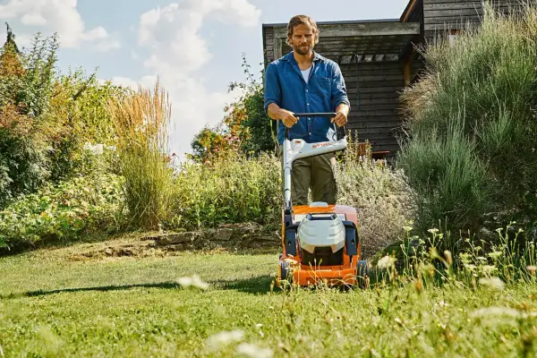 Uomo con tosaerba elettrico in un giardino rigoglioso. Il sole splende, un momento ideale per prendersi cura del prato, ma quando innaffiare il prato?