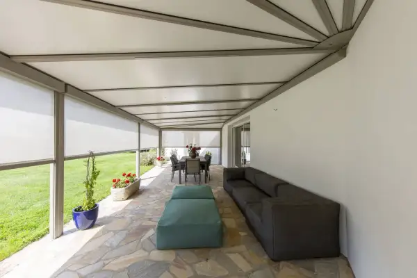 Telo per pergolato fissato con sistema a scomparsa, creando un'area relax con divano e tavola da pranzo.