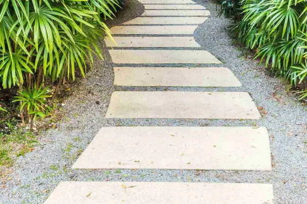 Un sentiero sinuoso in lastre di pietra su ghiaia, un'idea per come pavimentare un giardino senza cemento, circondato da vegetazione lussureggiante.