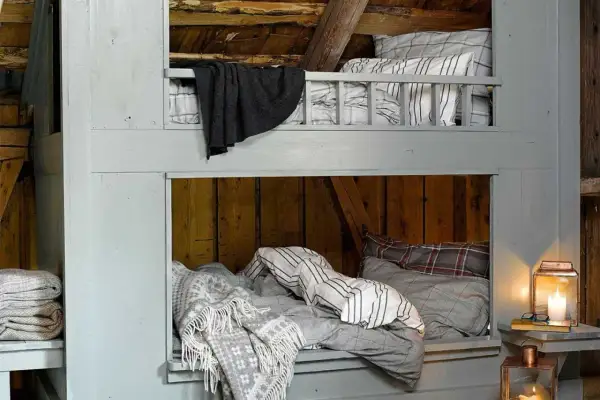 Accogliente letto a castello fai da te in legno grezzo, con coperte a quadri e a righe, perfetto per un rifugio rustico.
