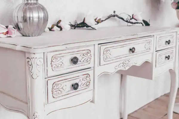 Un tavolo da toeletta bianco, con dettagli intagliati e un effetto invecchiato, pronto per essere restaurato in stile shabby.