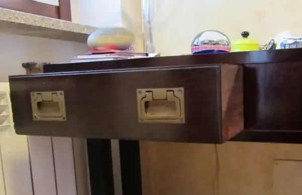 Cassetti che non scorrono, con maniglie dorate su un mobile scuro. Sul piano, oggetti decorativi e libri.