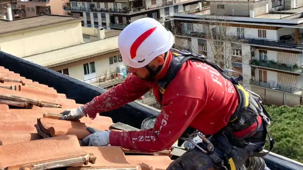 Operaio con imbracatura lavora sul tetto per isolare tetto senza togliere tegole, applicando materiale isolante.